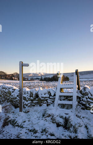 Footpath sign and wooden stile on a snowy winter morning near Rowarth in Derbyshire, England. Stock Photo