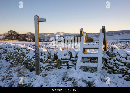 Footpath sign and wooden stile on a snowy winter morning near Rowarth in Derbyshire, England. Stock Photo