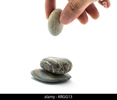 The stones are stacked and the hands are holding stones being laid on a pile of rocks on white background. Stock Photo