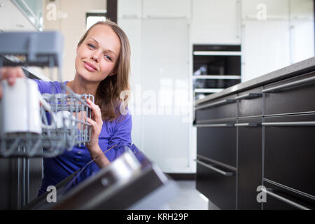 Pretty, young woman in her modern and well equiped kitchen putting cups into the dishwasher Stock Photo