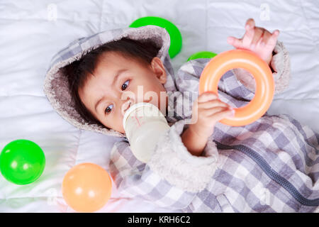 baby drinking milk with bottle on bed at home Stock Photo