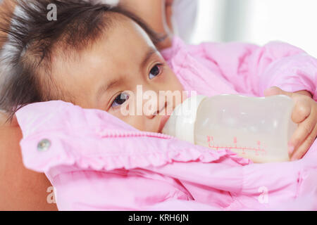 baby drinking a milk from bottle with mother on a bed Stock Photo