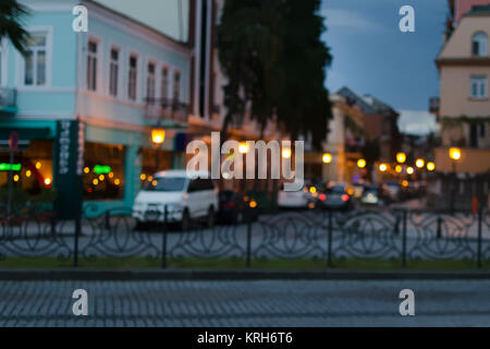 Blurred photo of small city street in the summer evening - stuck lights, cars, restaurants. Stock Photo