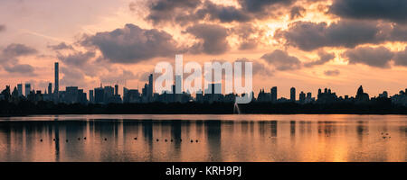 A pink winter sunset over Hell's Kitchen and Midtown with the buildings reflected in the Jaqueline keneddy Onassis reservoir in Central Park, Manhatta Stock Photo