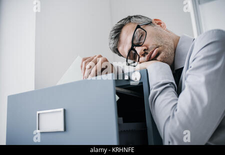 Tired lazy office worker leaning on a filing cabinet and sleeping, he is falling asleep standing up; stress, unproductivity and sleep disorders concep Stock Photo