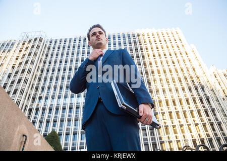 Young man in elegant suit posing with the laptop in his hand looking away. Stock Photo
