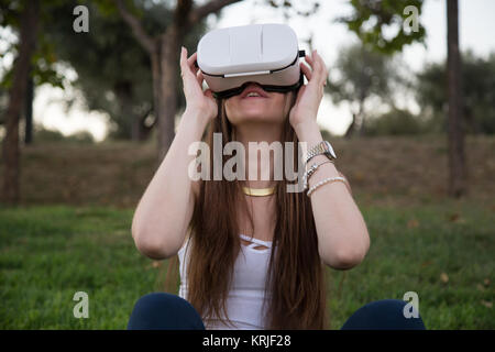 Smiling brunette having fun while using glasses of virtual reality in park. Stock Photo