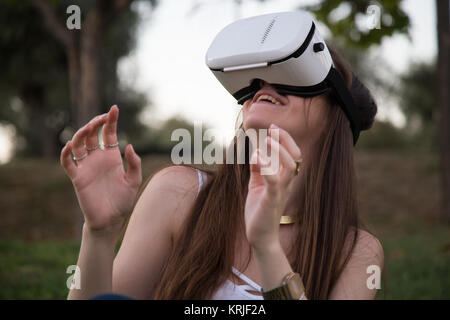 Smiling brunette having fun while using glasses of virtual reality in park. Stock Photo