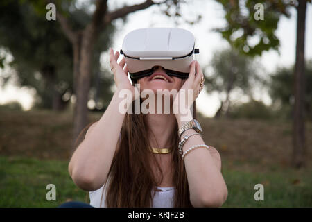 Smiling brunette having fun while using glasses of virtual reality in park. Stock Photo