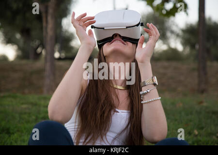 Smiling brunette having fun while using glasses of virtual reality in park. Stock Photo