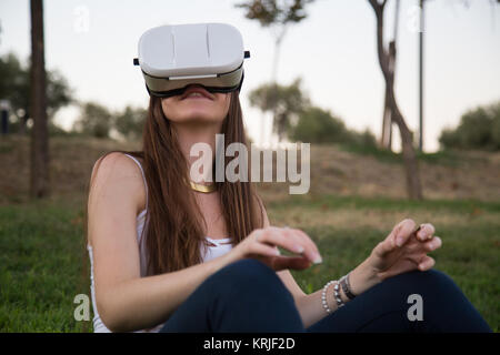 Smiling brunette having fun while using glasses of virtual reality in park. Stock Photo
