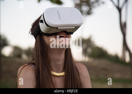 Smiling brunette having fun while using glasses of virtual reality in park. Stock Photo