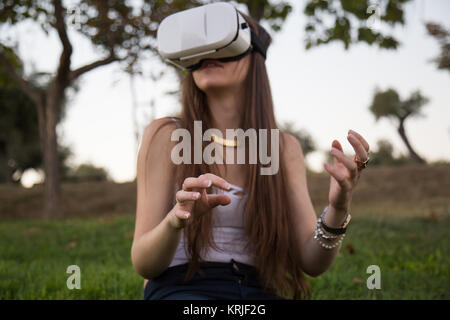 Smiling brunette having fun while using glasses of virtual reality in park. Stock Photo
