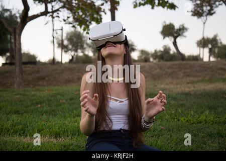 Smiling brunette having fun while using glasses of virtual reality in park. Stock Photo