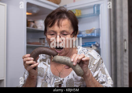 Surprised senior woman holding pork liver sausages Stock Photo