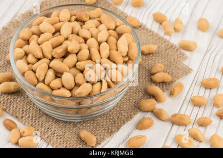 Salted peanuts in a glass bowl on the old wooden table. Stock Photo