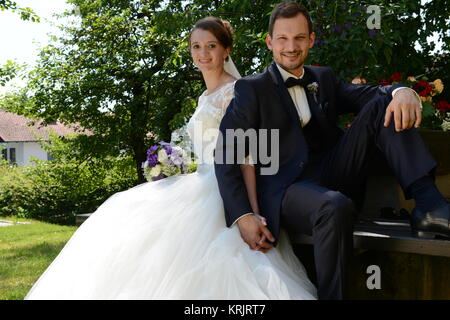 young bridal couple is sitting in the park on a park bench Stock Photo