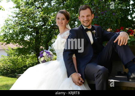 young bridal couple is sitting in the park on a park bench Stock Photo