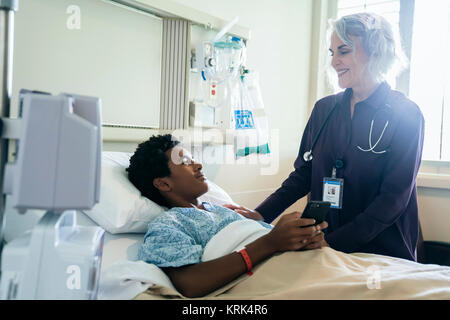 Doctor comforting boy in hospital bed holding cell phone Stock Photo