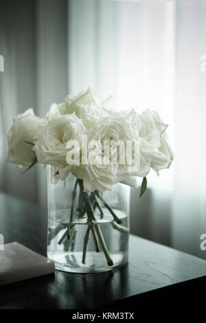 a vase of white roses and a book on the table Stock Photo