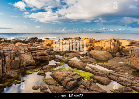 The orange-red granite of the Thorr Pluton on the foreshore at Bloody Foreland, County Donegal, with Tory Island in the background Stock Photo