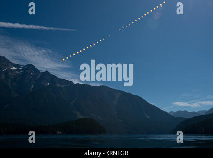This composite image shows the progression of a partial solar eclipse over Ross Lake, in Northern Cascades National Park, Washington on Monday, Aug. 21, 2017. A total solar eclipse swept across a narrow portion of the contiguous United States from Lincoln Beach, Oregon to Charleston, South Carolina. A partial solar eclipse was visible across the entire North American continent along with parts of South America, Africa, and Europe.  Photo Credit: (NASA/Bill Ingalls) 2017 Total Solar Eclipse (NHQ201708210306) Stock Photo