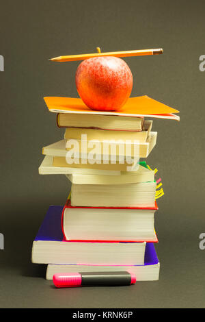 Concept of education. Stack of school books with pink marker, pencil and a red apple on top in front of dark gray background Stock Photo