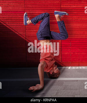 Break dancer doing handstand against red wall background Stock Photo
