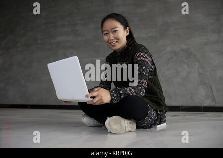 Woman sitting on the floor  holding a laptop and smiling Stock Photo