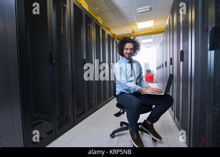 Young technician working on a laptop next to black server racks Stock Photo