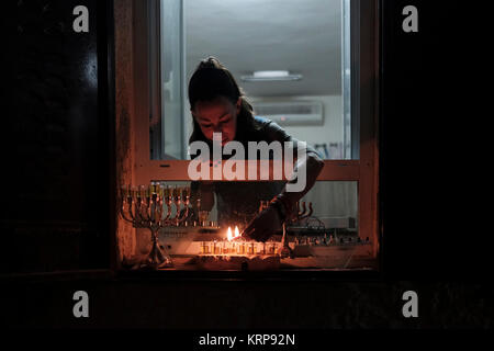 A religious Jewish woman lights an olive oil candle on a menorah candelabrum placed on the windowsill of her house during the Jewish holiday of Hanukkah, the festival of lights, at the Jewish Quarter in Old city Jerusalem Israel Stock Photo