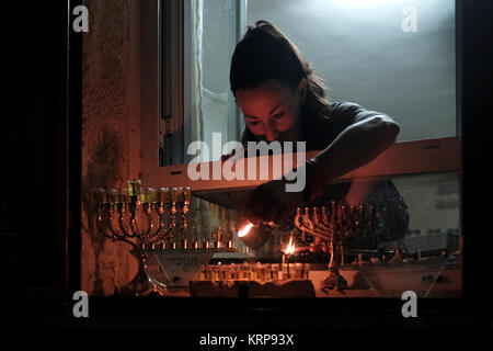 A religious Jewish woman lights an olive oil candle on a menorah candelabrum placed on the windowsill of her house during the Jewish holiday of Hanukkah, the festival of lights, at the Jewish Quarter in Old city Jerusalem Israel Stock Photo