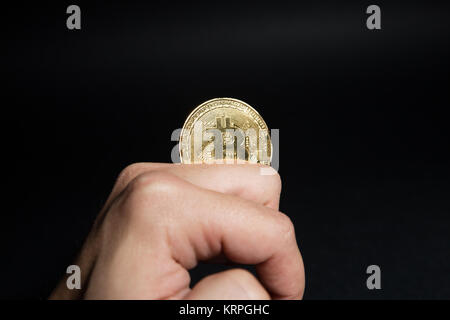 Male hand playing with golden Bitcoin between fingers on dark black background Stock Photo