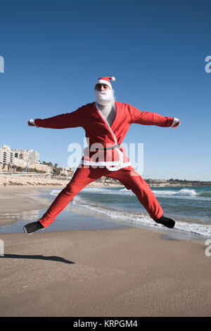 a young man in a santa suit jumping on the beach Stock Photo