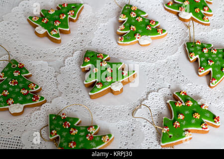 Painted gingerbread in the shape of Christmas tree on a white napkin background. Christmas trees cookies - colorful icing decoration. Stock Photo