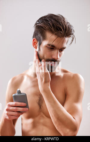 Young man is applying aftershave to his face. Stock Photo