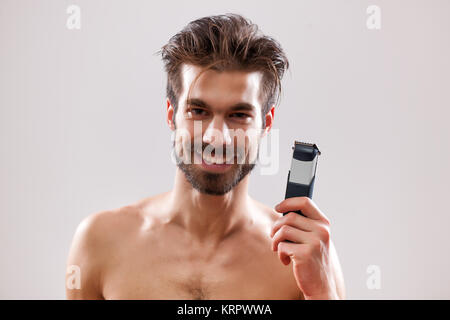 Young man is holding electric razor and he is going to shave his beard. Stock Photo