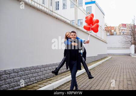 Girl piggyback on guy with red heart balloons on the street.  Stock Photo