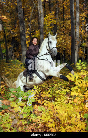 Young woman and her beautiful white arabian stallion rearing up in the autumn woods Stock Photo