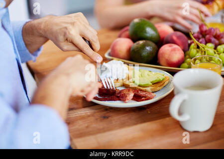 man with fork eating bacon at table full of food Stock Photo