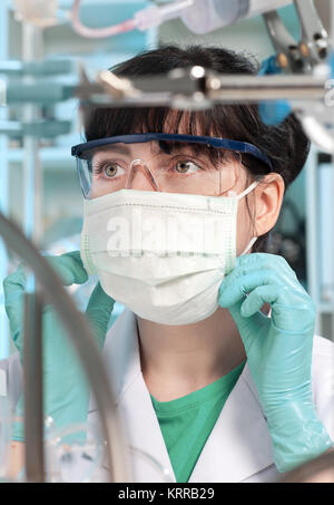Female tech in protective wear puts a mask on Stock Photo