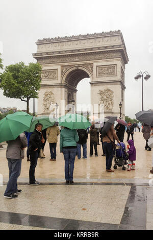 View of the Arc de Triomphe from the western end of the Champs-Elysees on a rainy day, with many people standing around holding umbrellas, three green Stock Photo