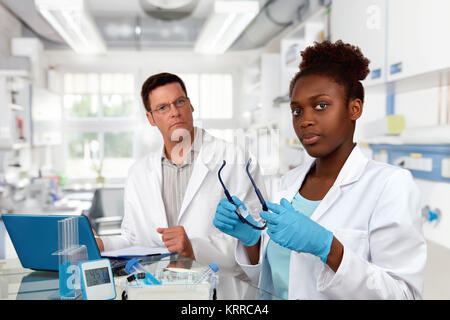 Scientists, senior Caucasian male and young African female, work in research facility. Focus on the woman. Stock Photo