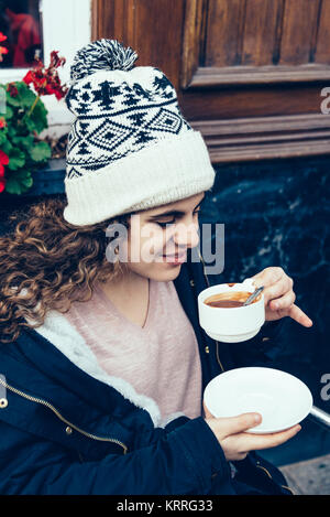 A teenage girl is sitting in a terrace and is drinking a cup of  Stock Photo