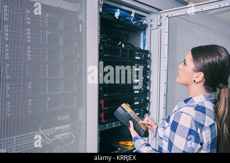 female technician working on server maintenance in white server room next to open server rack Stock Photo