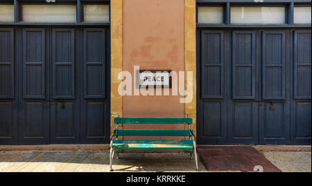 Word peace framed above an old wooden bench on a column between two locked doors. Close up view. Stock Photo