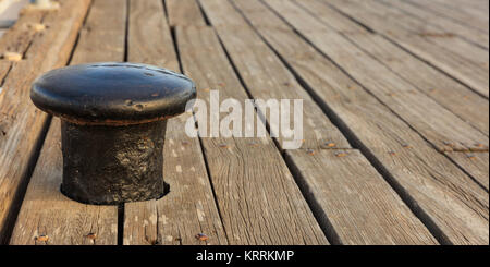 Black rusty bollard mooring on wooden deck background. Blurred, closeup view with details. Copy space Stock Photo