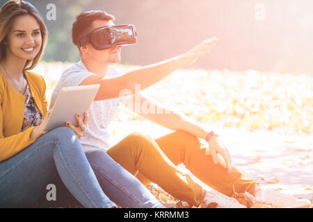 Couple sitting outside using various tech gadgets, tablet, vr, concept Stock Photo