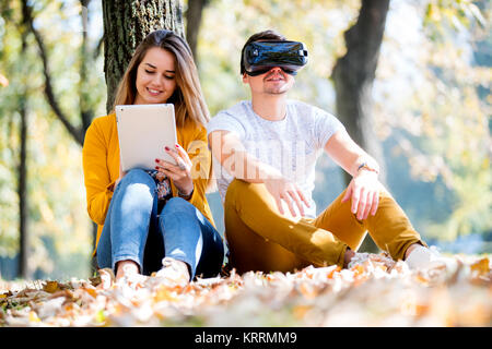 Couple sitting outside using various tech gadgets, tablet, vr, concept Stock Photo