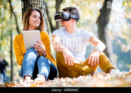 Couple sitting outside using various tech gadgets, tablet, vr, concept Stock Photo